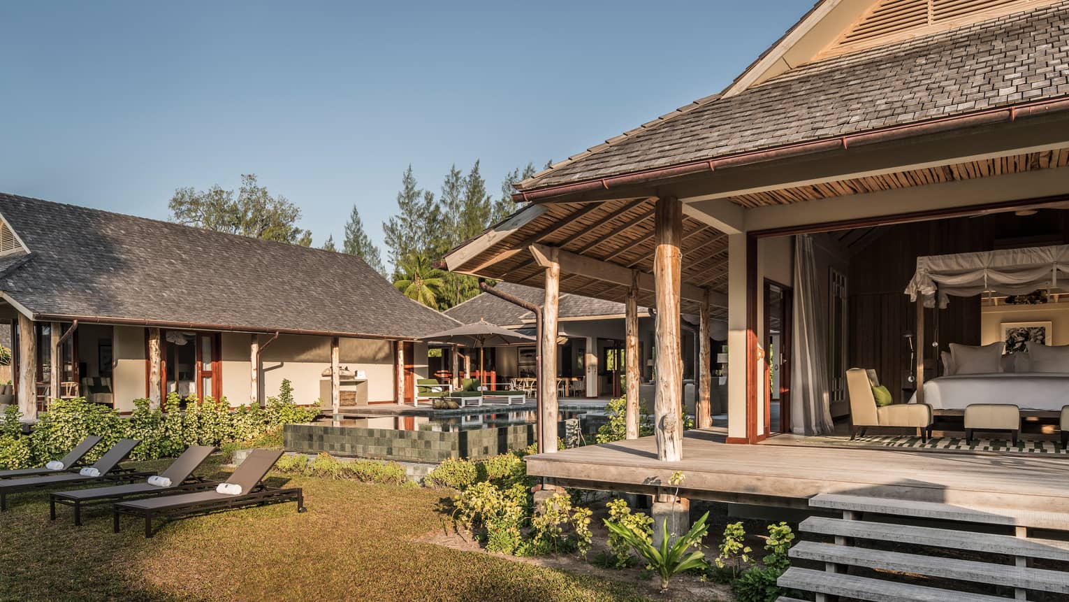 View of bungalow patio, open wall to bedroom from lawn with lounge chairs