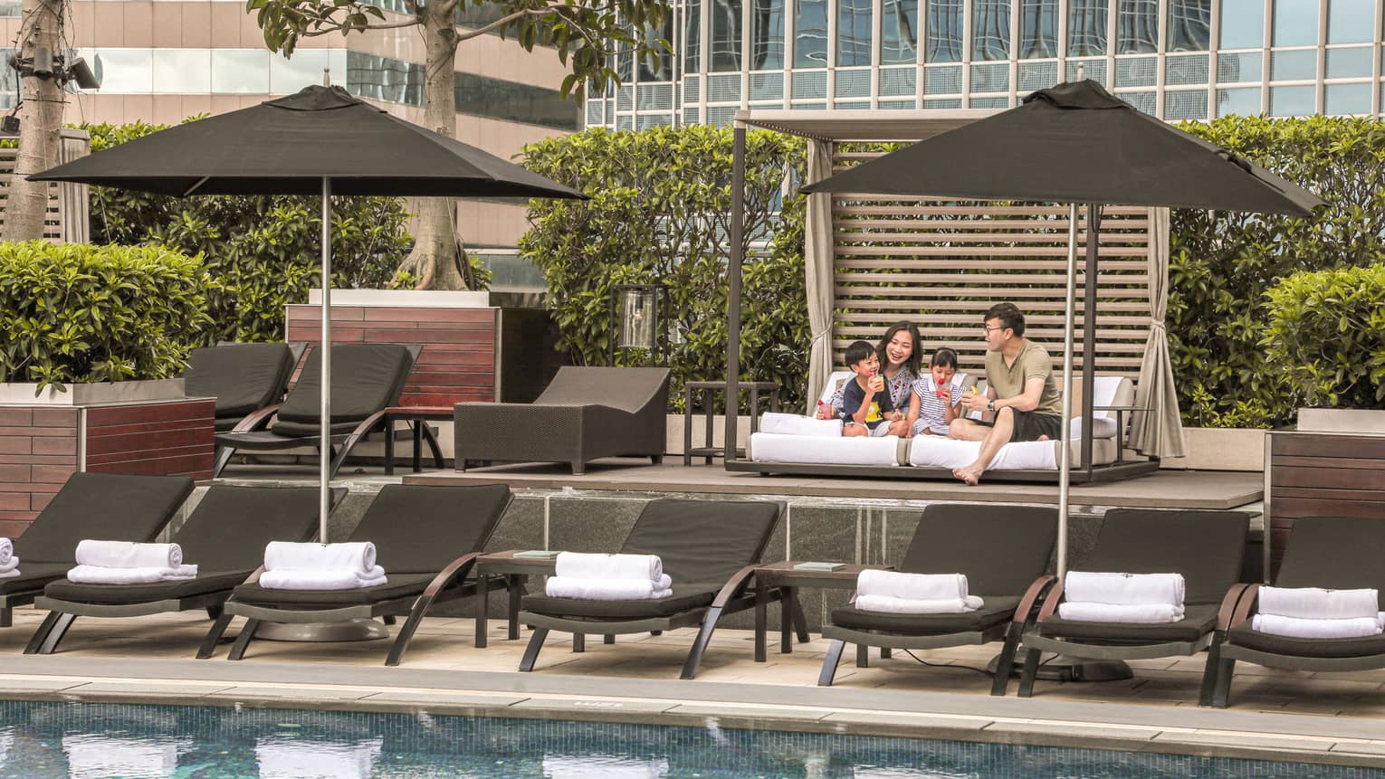 A mother, father and two young boys on daybed by pool