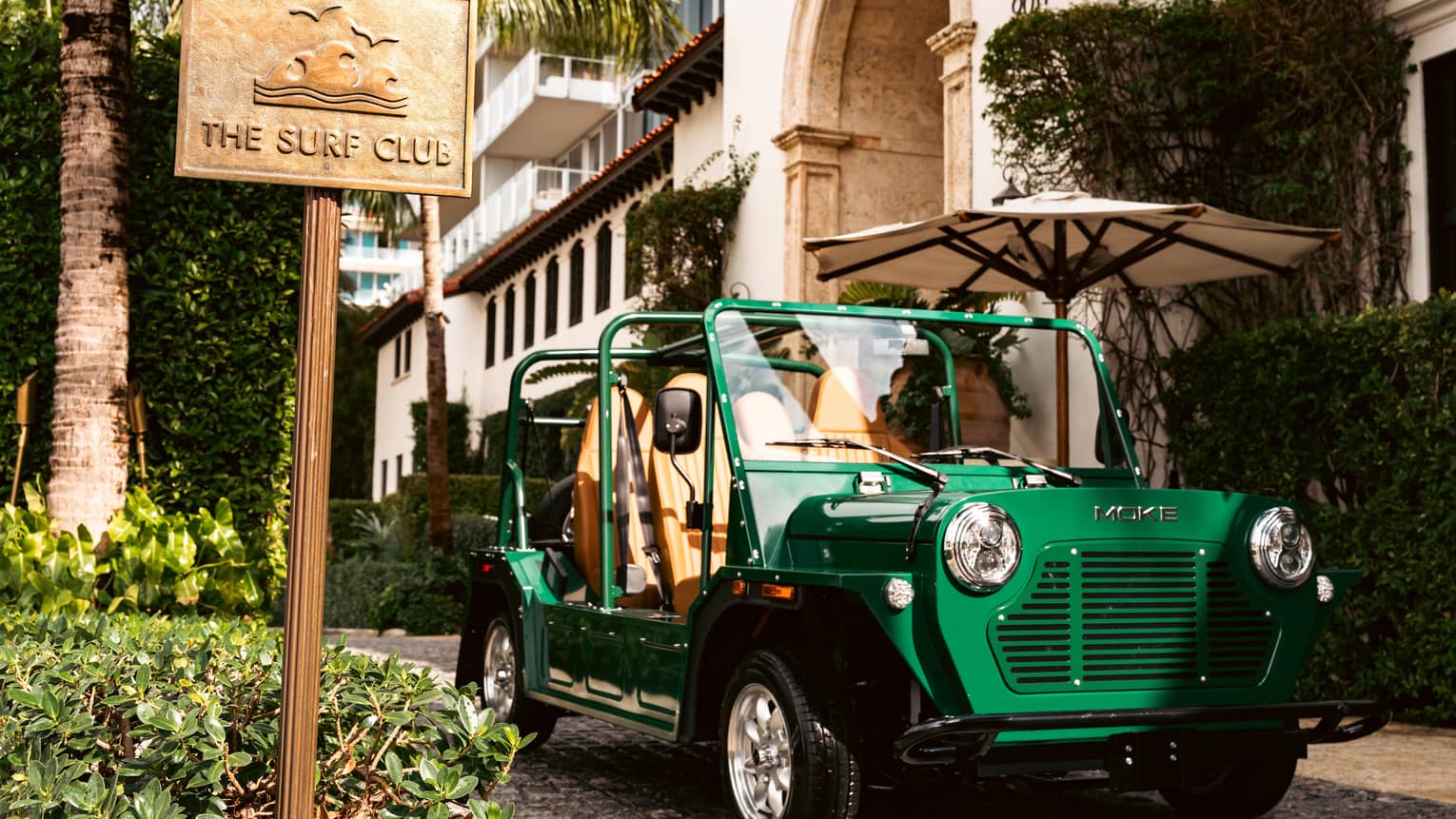 Green MOKE car parked outside of the building next to "The Surf Club" sign.