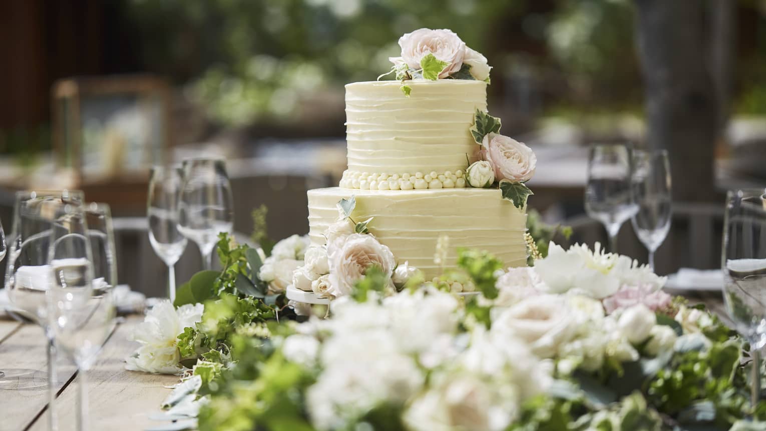 Two-tiered white wedding cake on banquet table with wine glasses, flowers