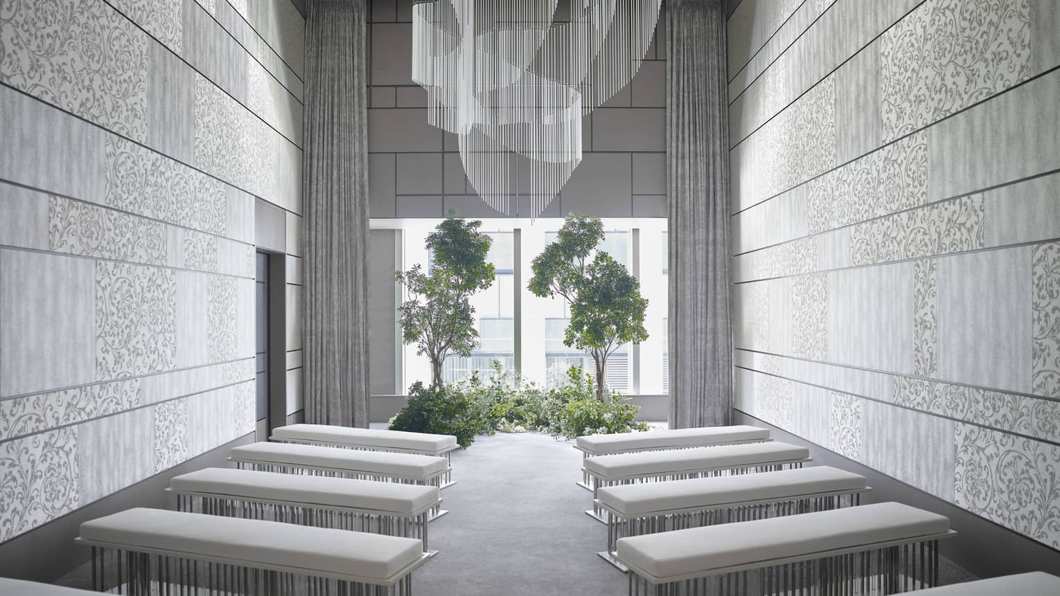 Modern event room, rows of plush benches face window and potted trees