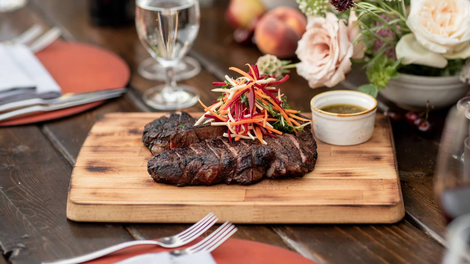 A steak on a wooden board near flowers.