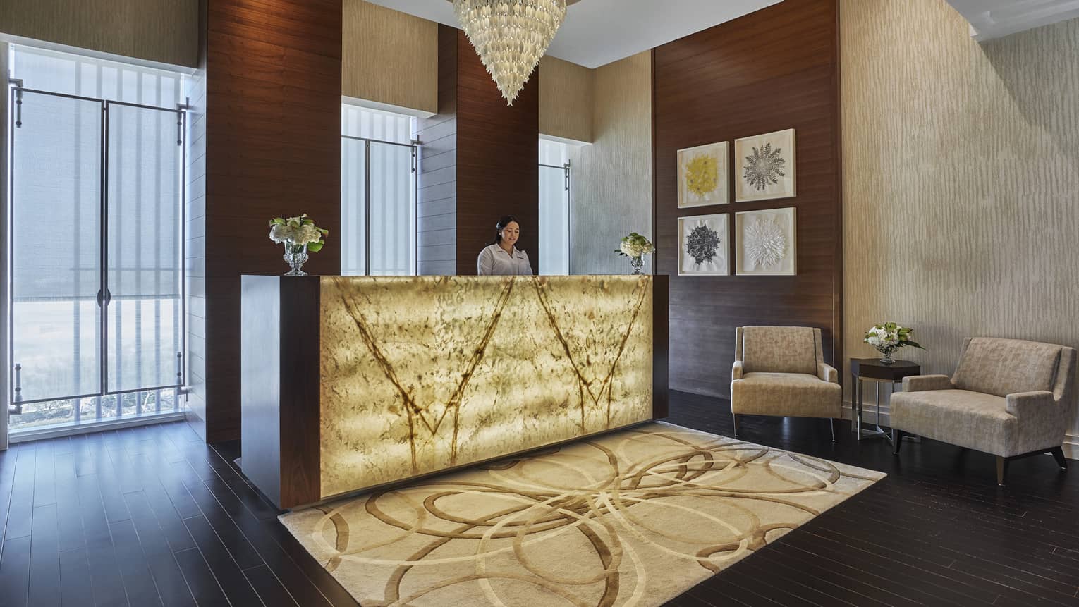 A yellow glass chandelier hangs over the welcome desk, adorned with soft yellow light and a brown rug.