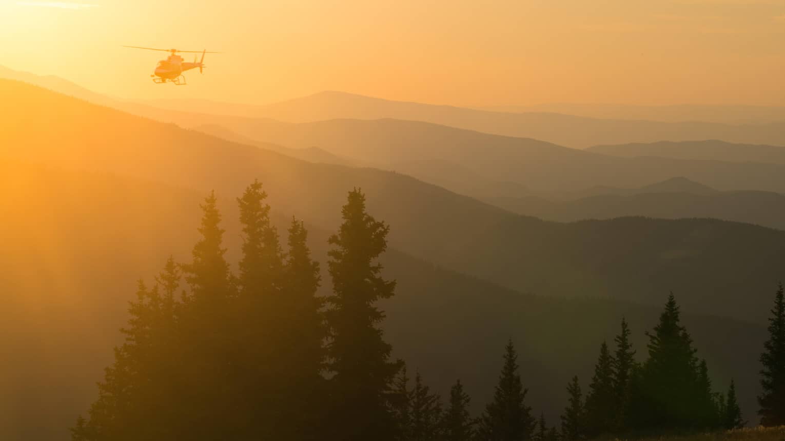 Helicopter at sunset flying over Aspen Mountain in the Elks Mountain range