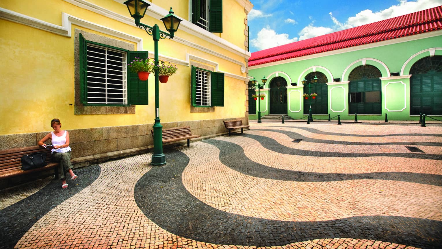 Female visitor sitting on bench outdoors in front of yellow and green buildings