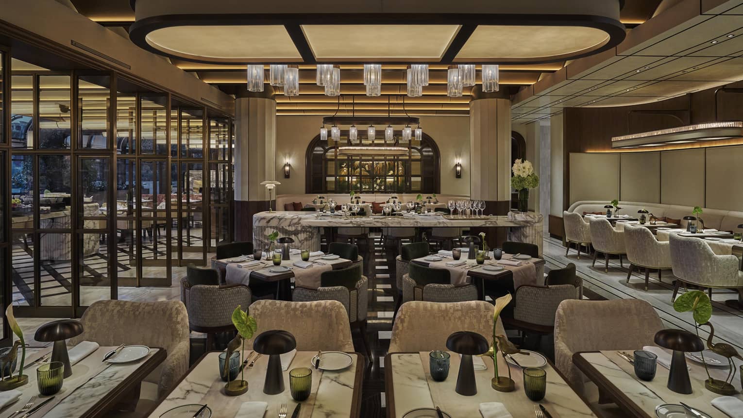 Restaurant dining room with grey and cream colour palatte, green florals on every table and a large overhead curved light piece