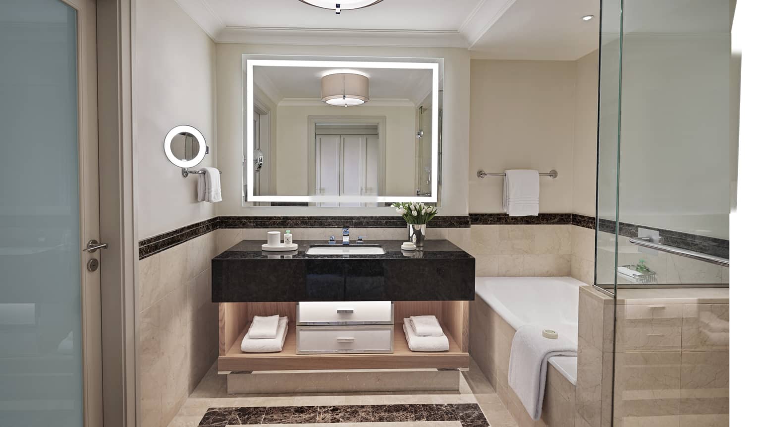 Bathroom with lighted mirror, black marble vanity, tub and separate glass shower
