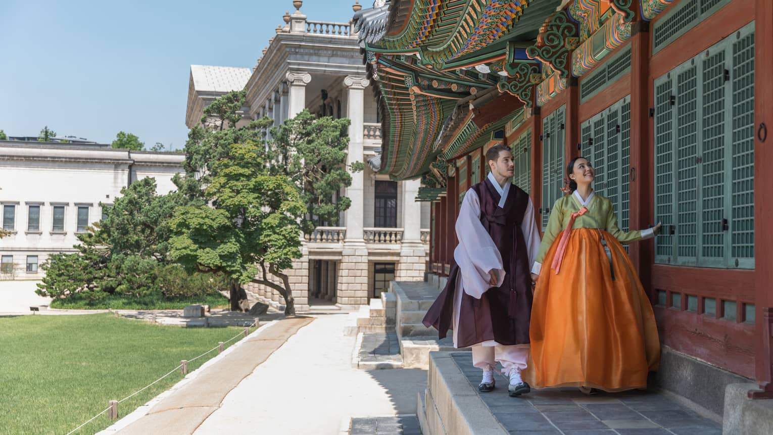 Man and woman in traditional Korean attire walk along the wall of a local palace