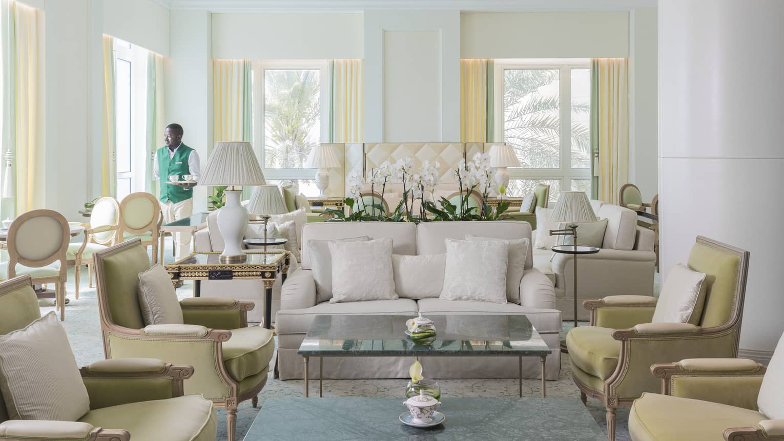 Light-filled tea lounge room, with white sofa, light yellow arm chairs, crown molding