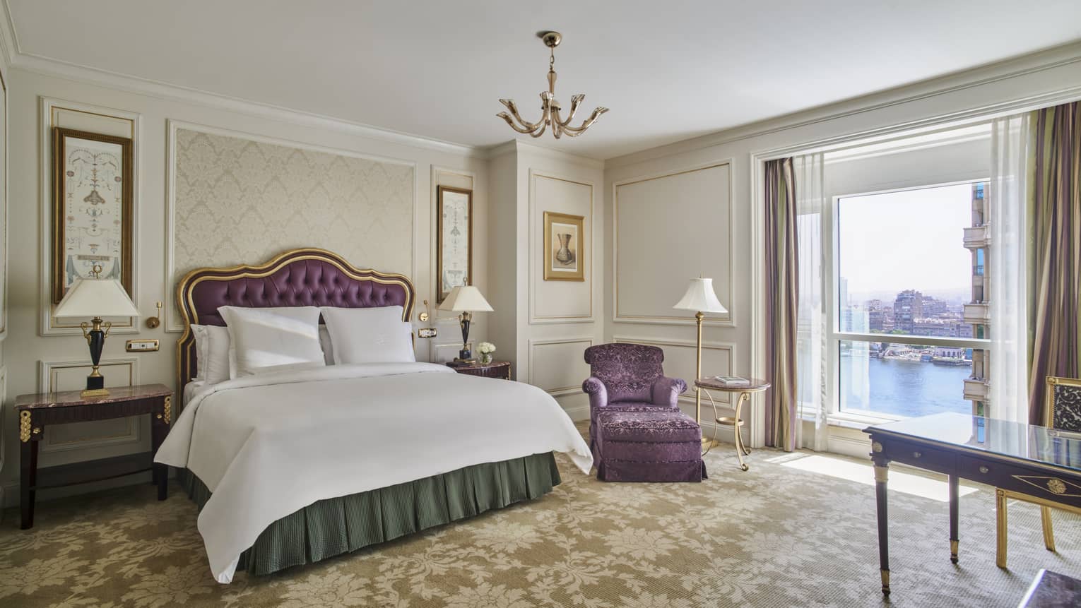 Hotel bedroom with elegant king bed, chaise, desk and Nile River view