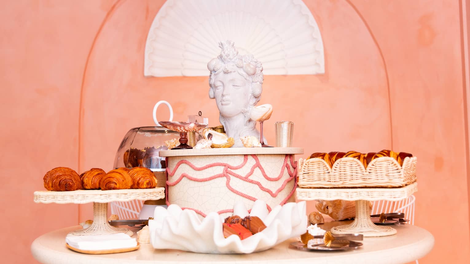 A display of pastries on a round table, with a Roman head of a woman as art