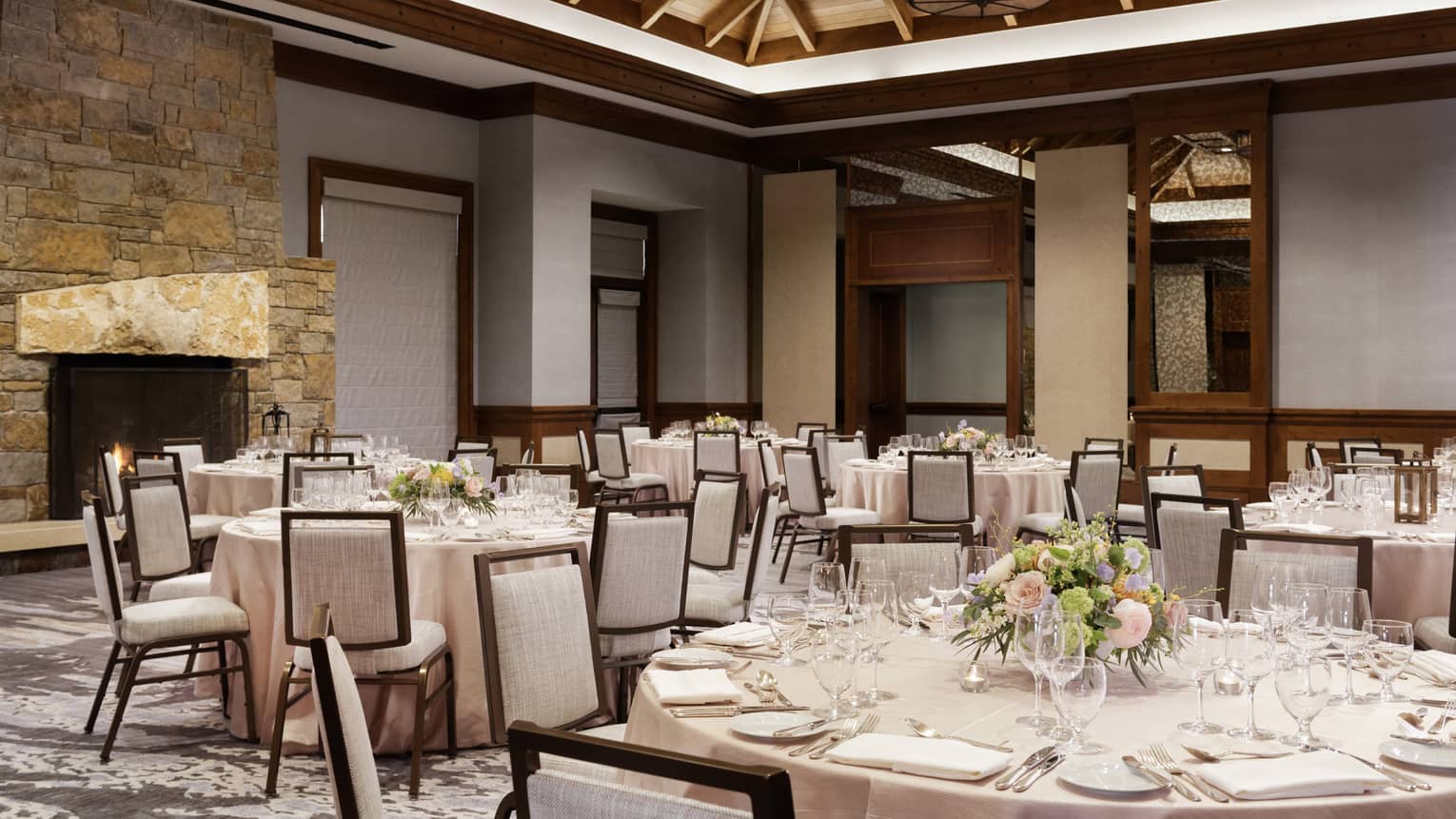 A large room with wood details, round tables with table cloths and grey chairs.