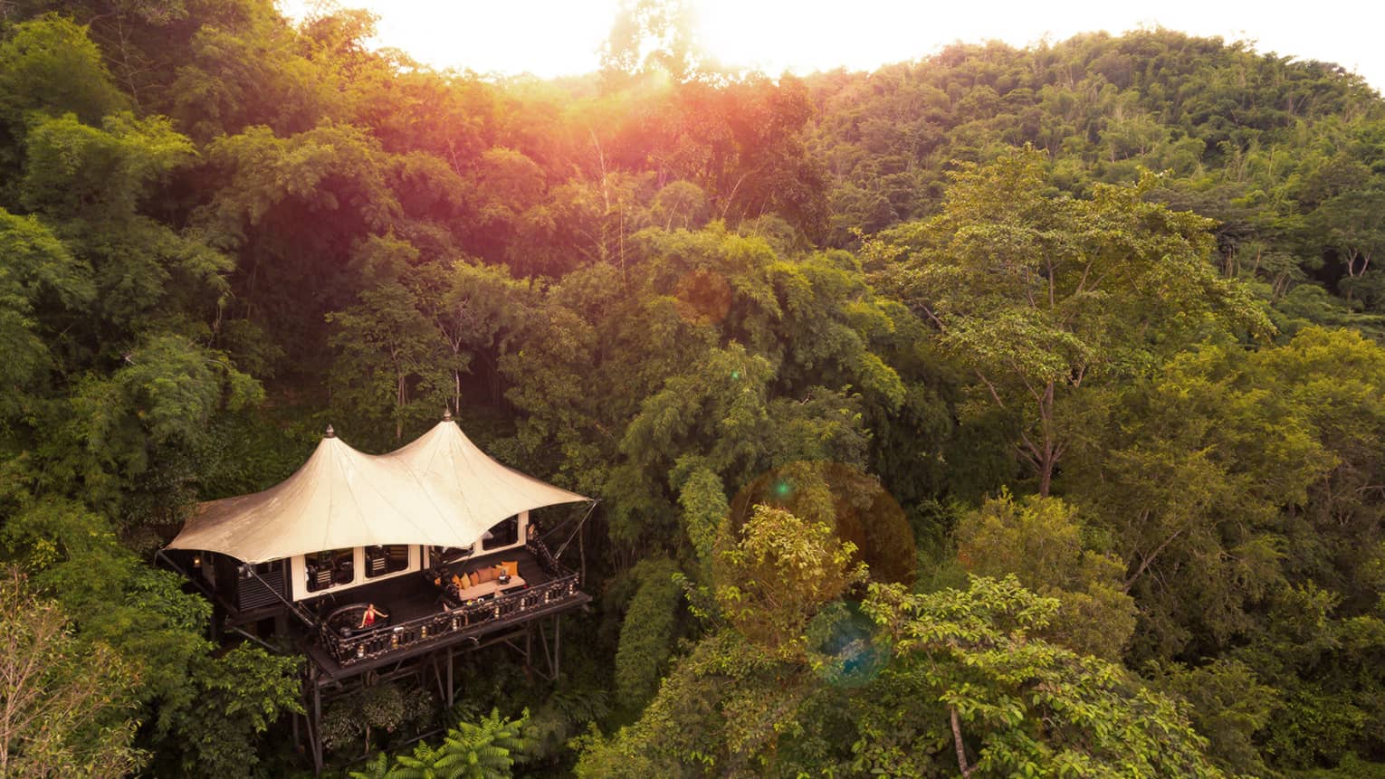 Small bungalow on lush tropical green mountain with golden sun behind trees