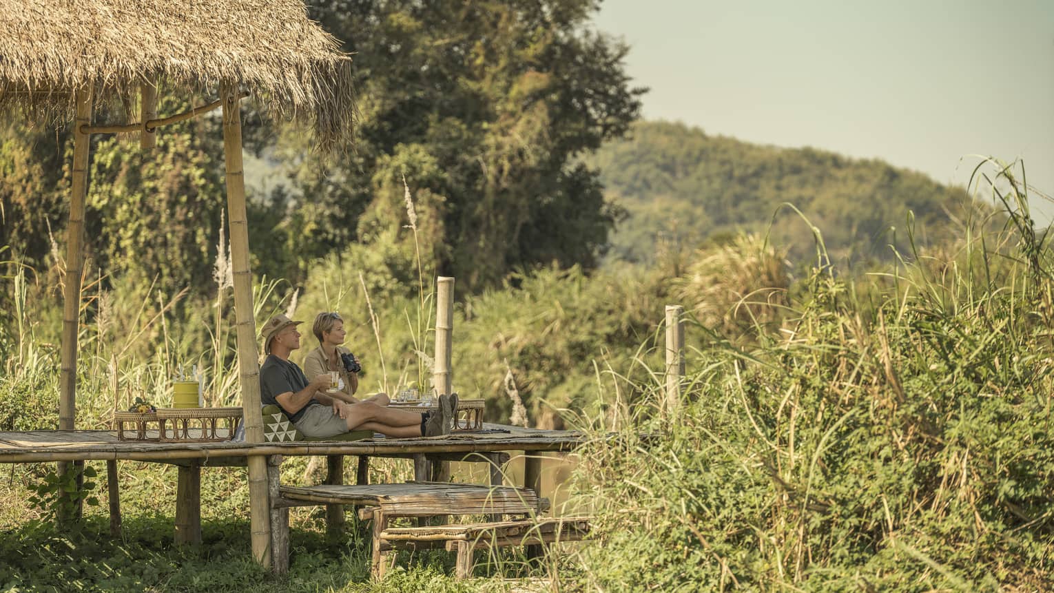 Camp Picnic, couple leans back against hut in jungle