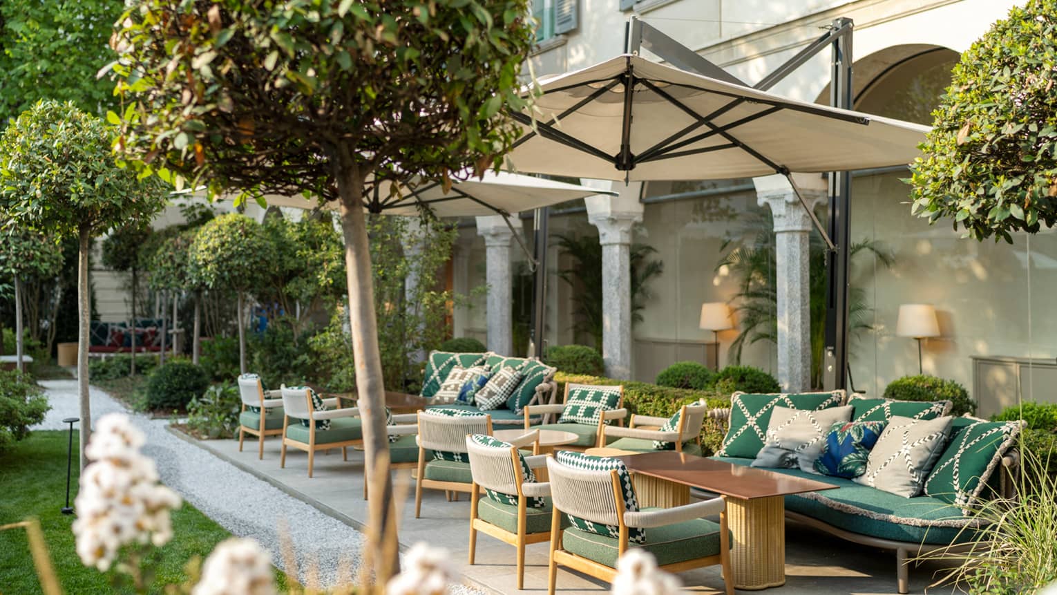 An outdoor seating area with umbrellas and green chairs surrounded by small trees.