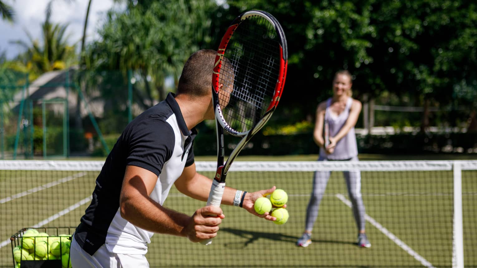 Couple playing tennis on court, man prepares to serve tennis balls to woman ready to swing