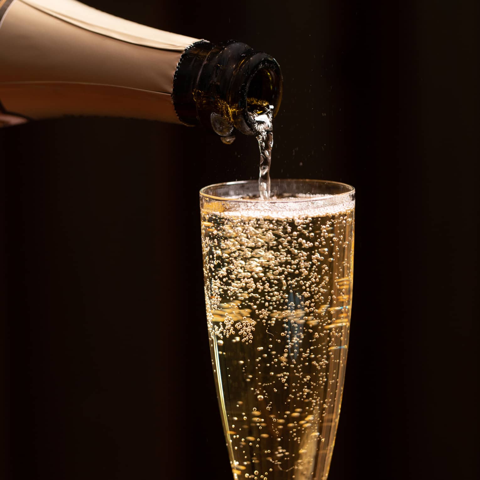 A bottle of champagne is poured into a glass as bubbles float to the top