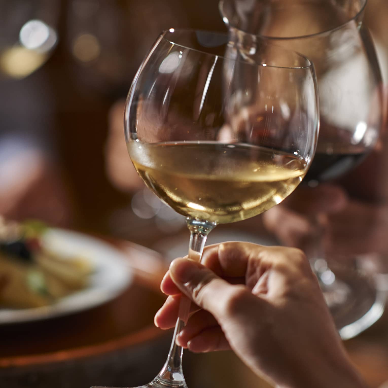 Two guests clink their wine glasses together at dinner