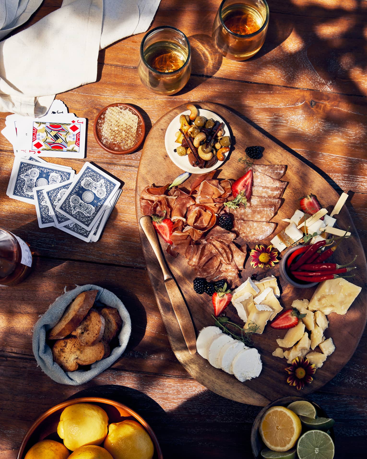 An assortment of cheese and bread and drinks on a table with playing chards.