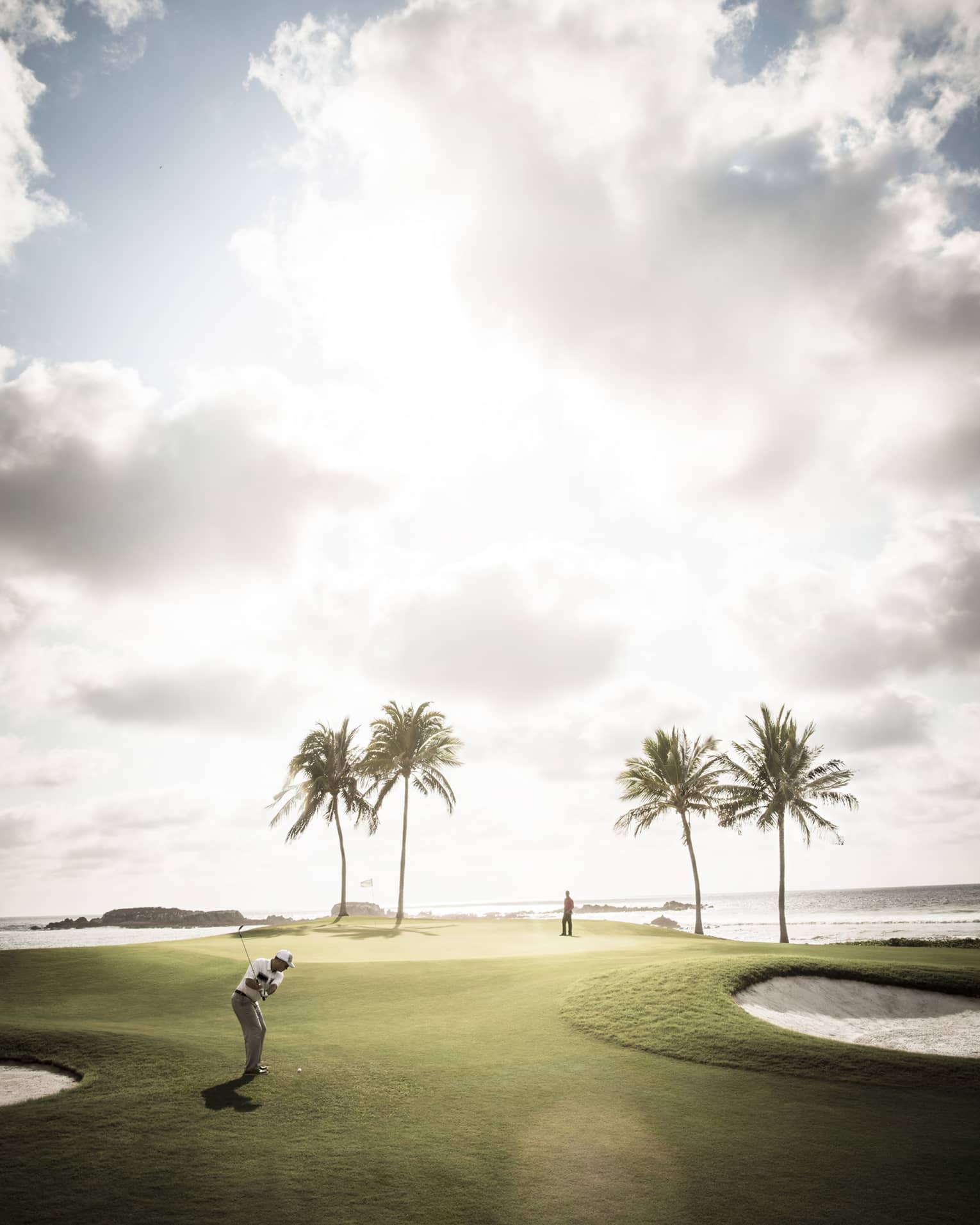 Man swings golf club on sunny course green with four palm trees