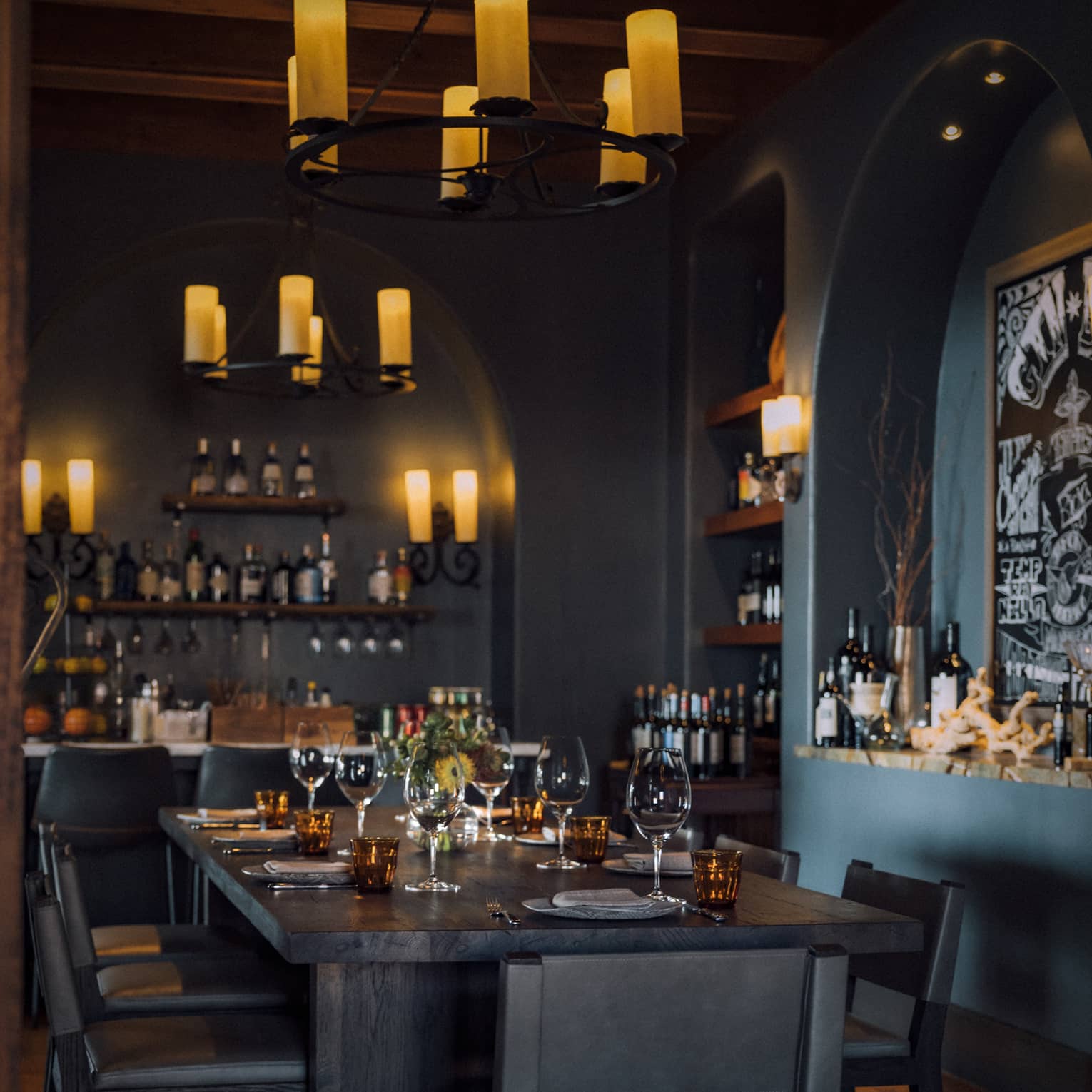 Dining room with candle light chandeliers and shelves of wine bottles.