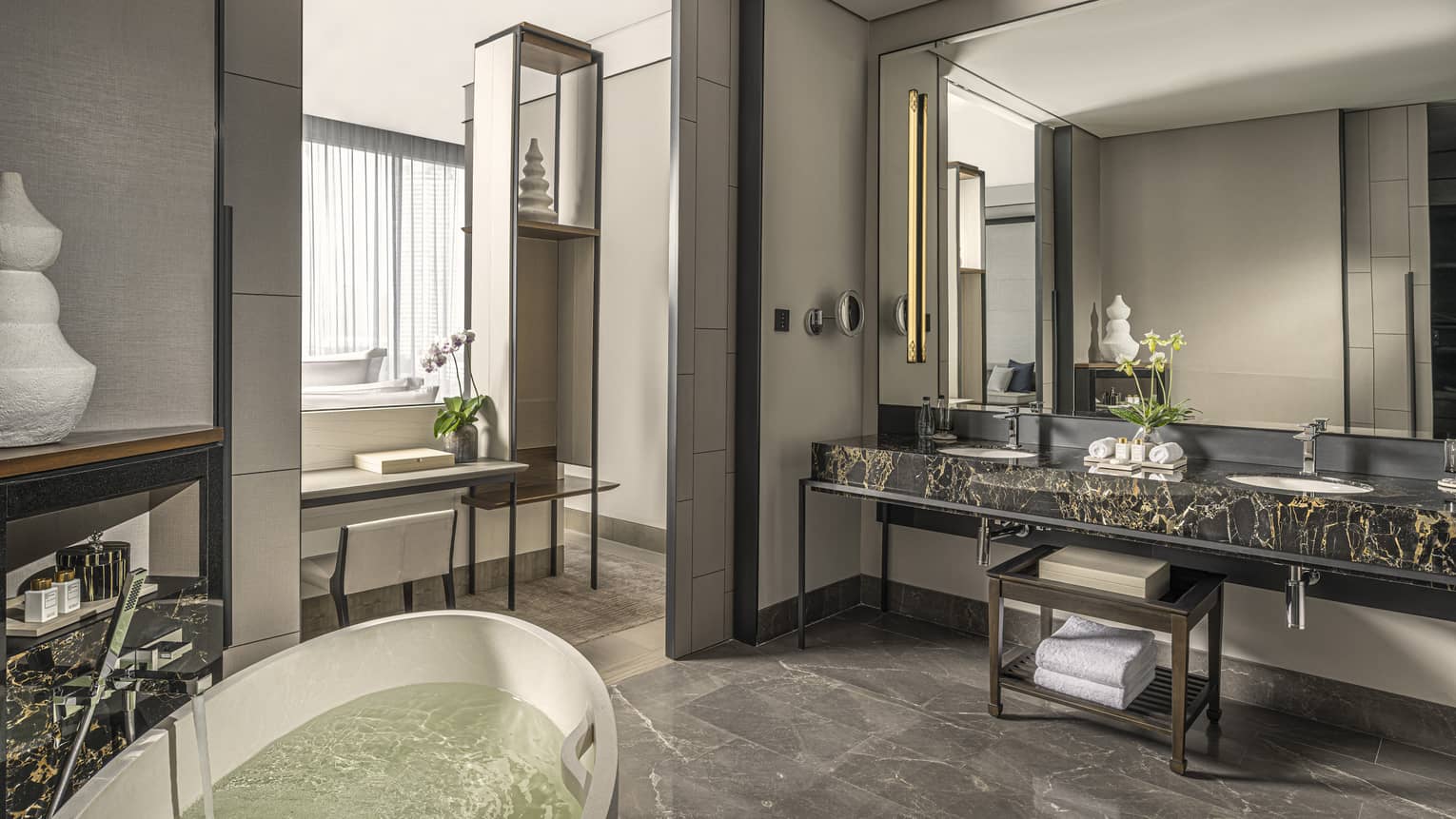 Bathroom, large mirror over black marble double vanity, standalone white tub, opening to bedroom
