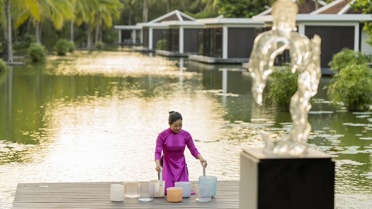 Woman plays crystal singing bowls on the dock of the lake