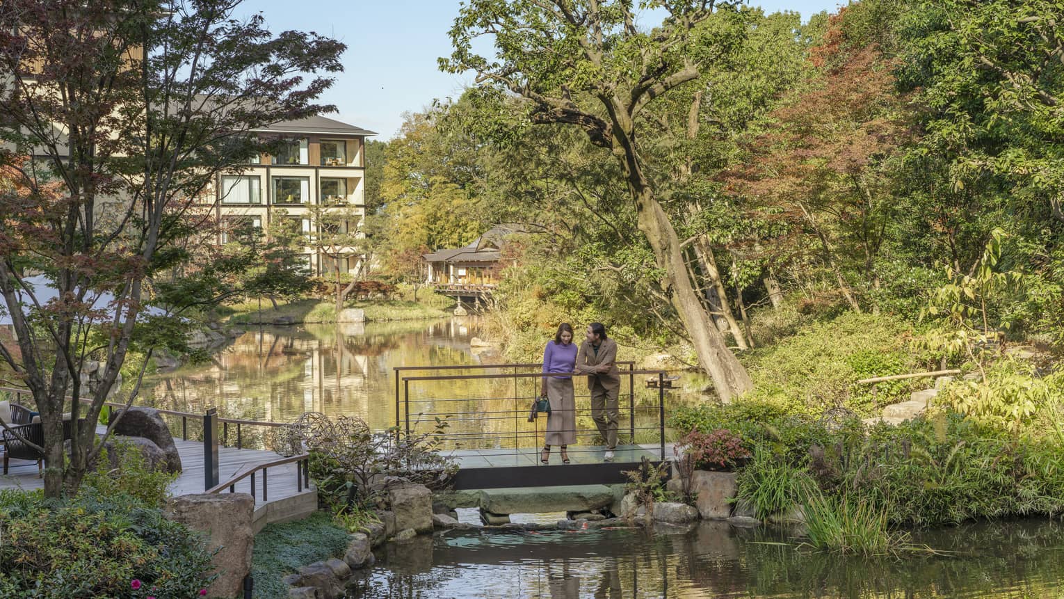 Couple stands on foot bridge overlooking koi pond