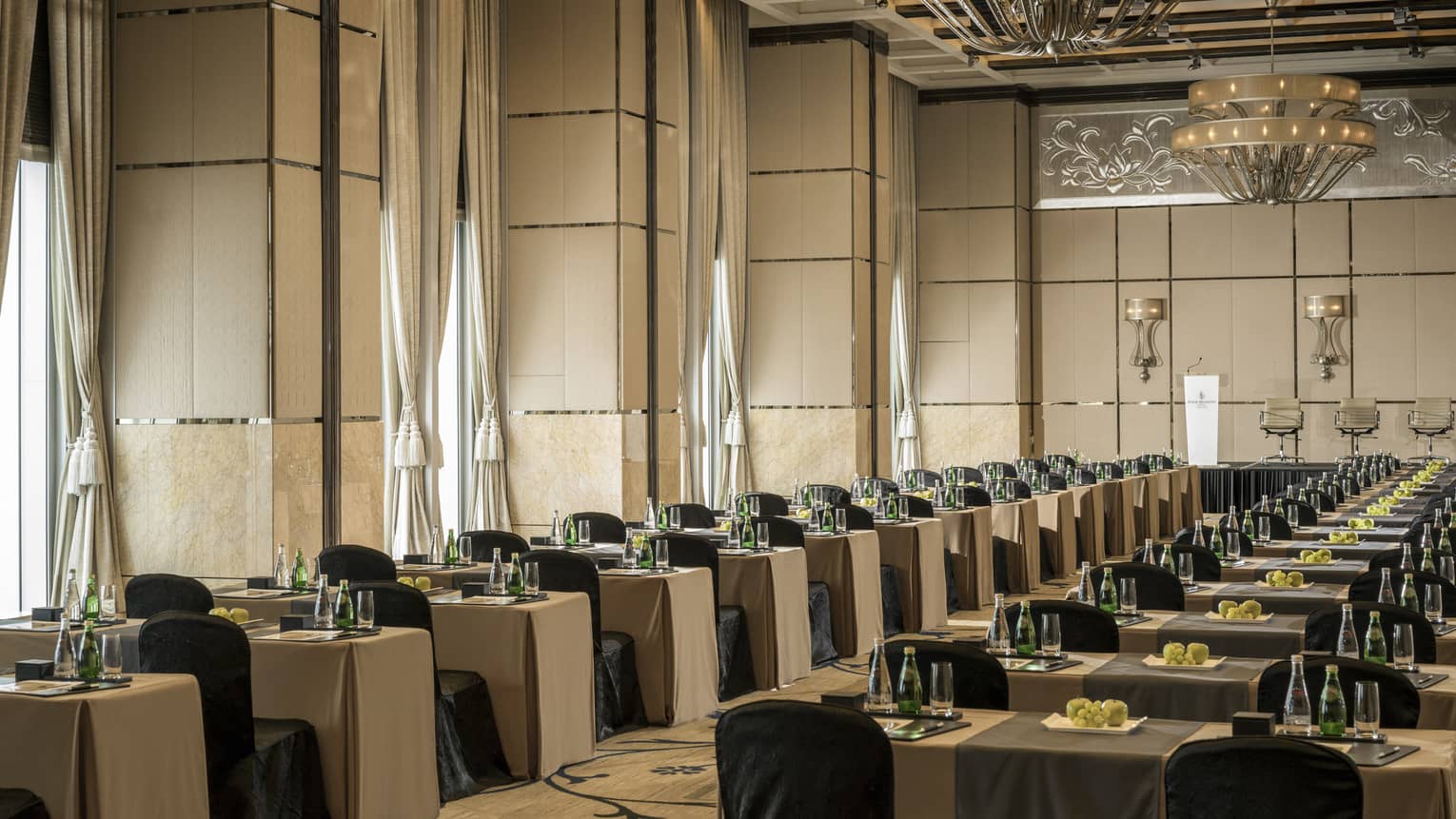 Rows of conference tables and chairs under high ceilings, tall windows in large ballroom