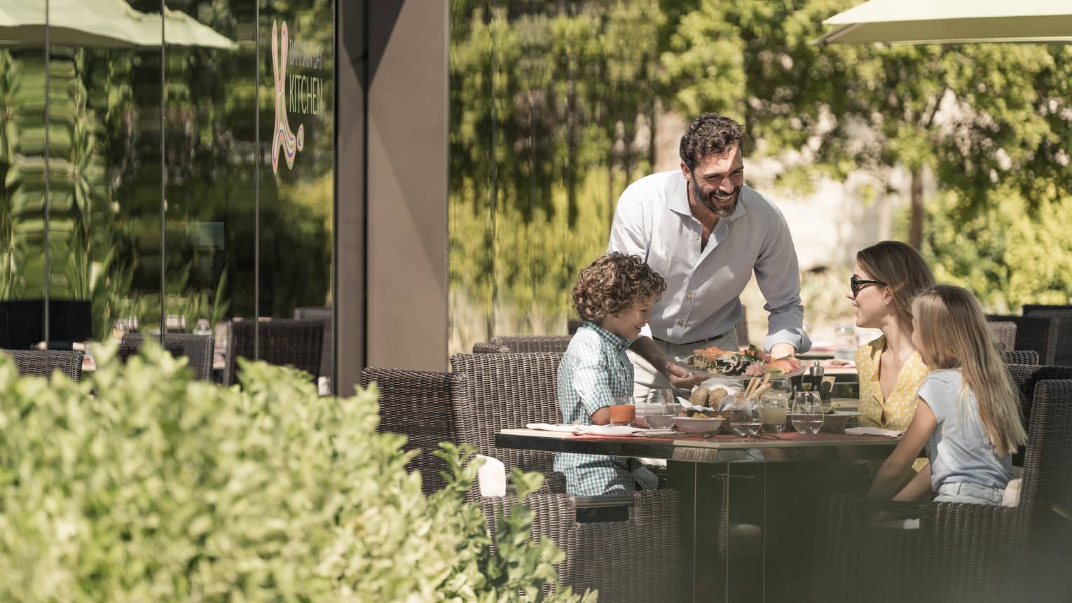 Family of four smiling at outdoor patio table over a meal