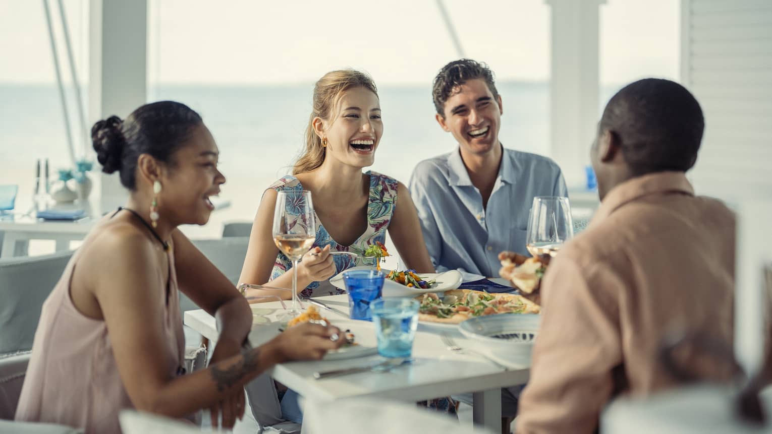 Two couples laugh as they share a meal at Blu Beach Club