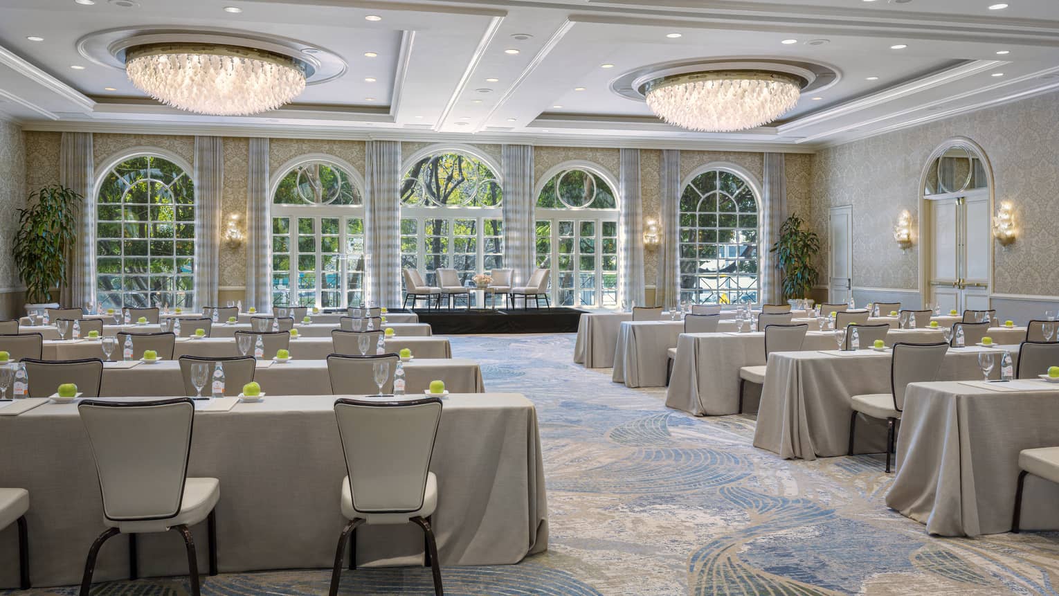 Ballroom set classroom style with cream-coloured linens, dual chandeliers, lighted wall sconces and floor-to-ceiling windows