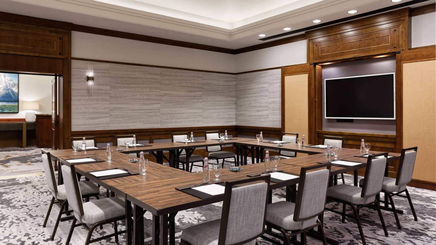 A meeting room with a large square table, chairs and a screen on a wall.