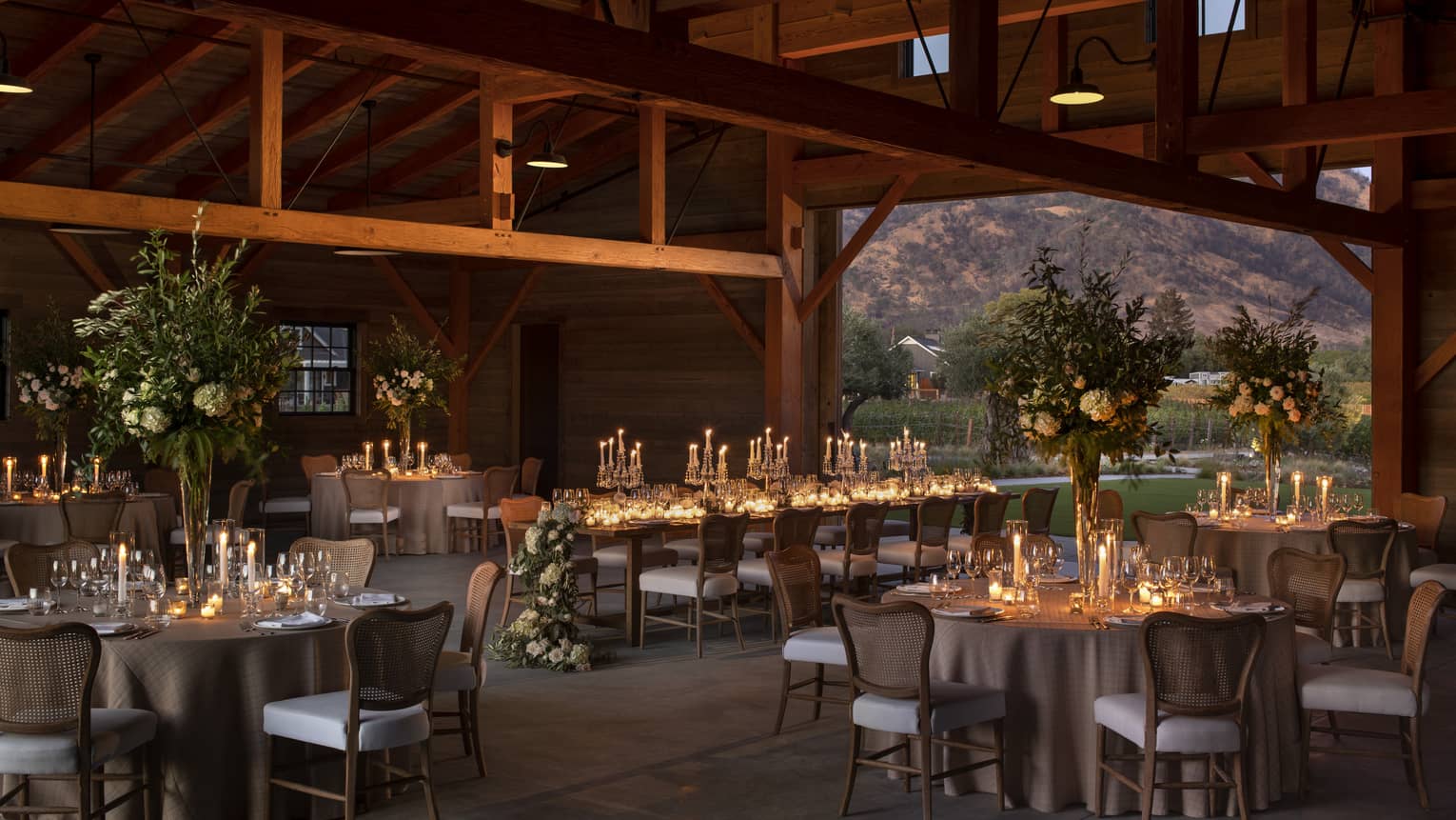 A beautifully arranged barn wedding reception, featuring tables and chairs under soft, dim lighting.