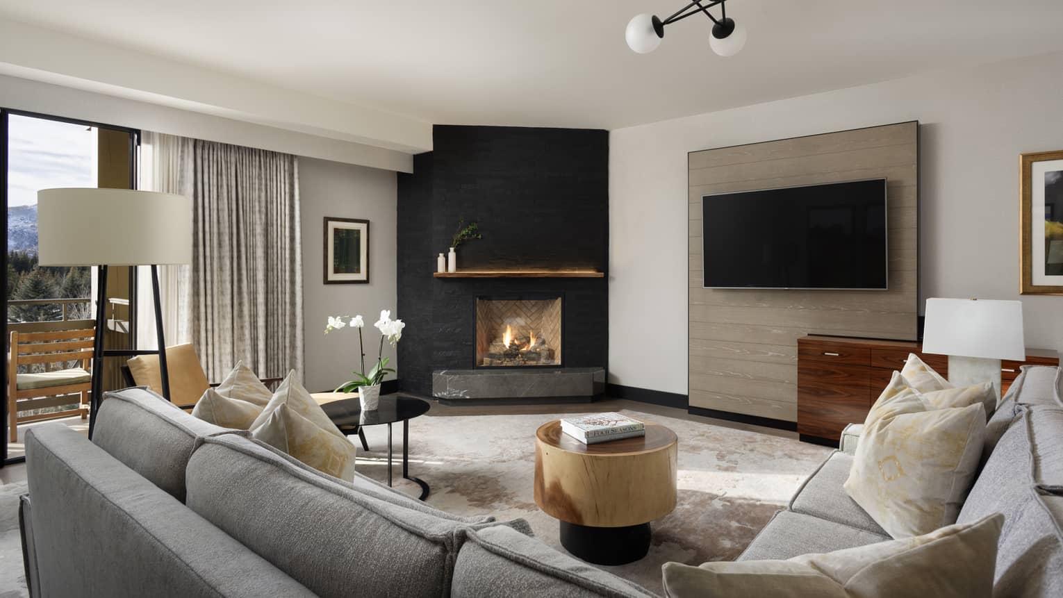Contemporary living room of hotel suite, featuring a TV, fireplace and grey sectional sofa