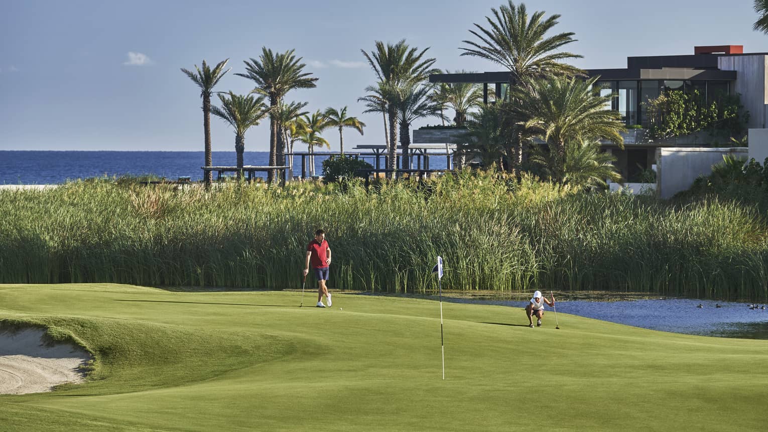 Two golfers enjoy a day on the golf course at four seasons Los Cabos with palm trees and the ocean in the background