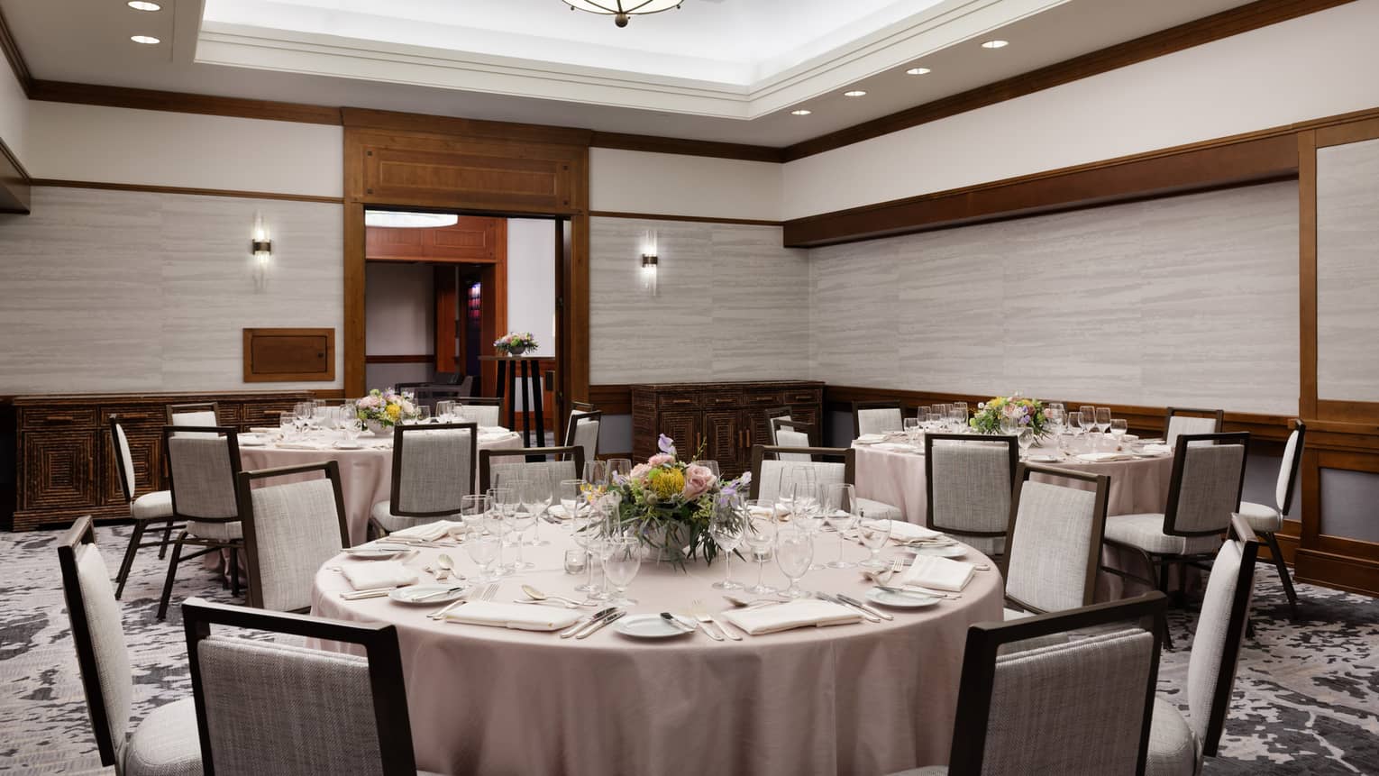 A room with large round tables with table cloths and grey chairs.