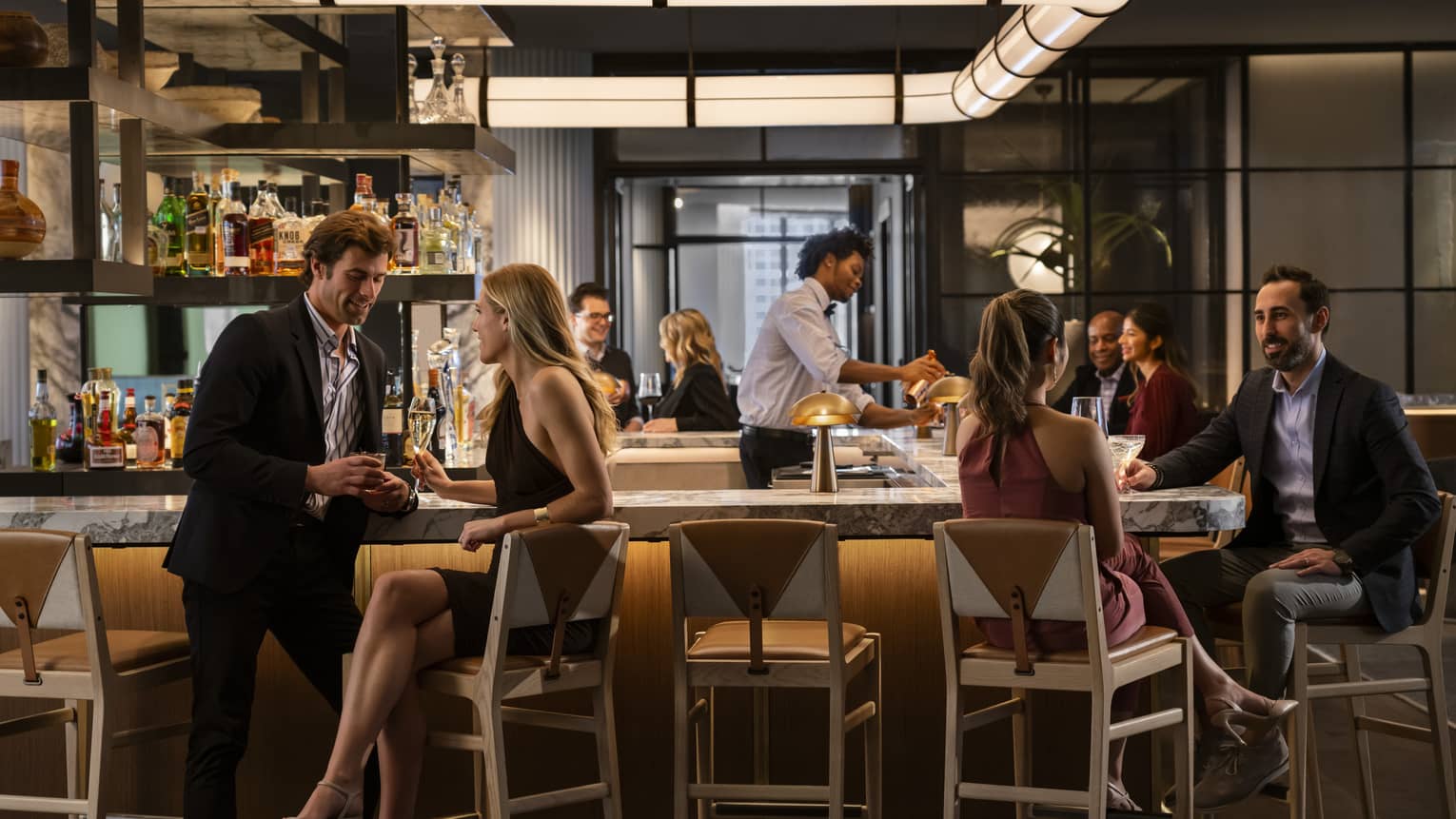 A bar area of a restaurant that is dimly lit with scattered groups of people sitting around it.