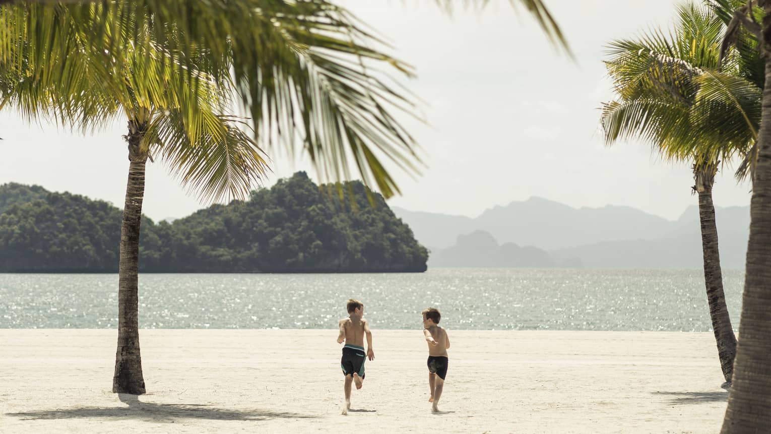 Two boys running toward the ocean on the beach