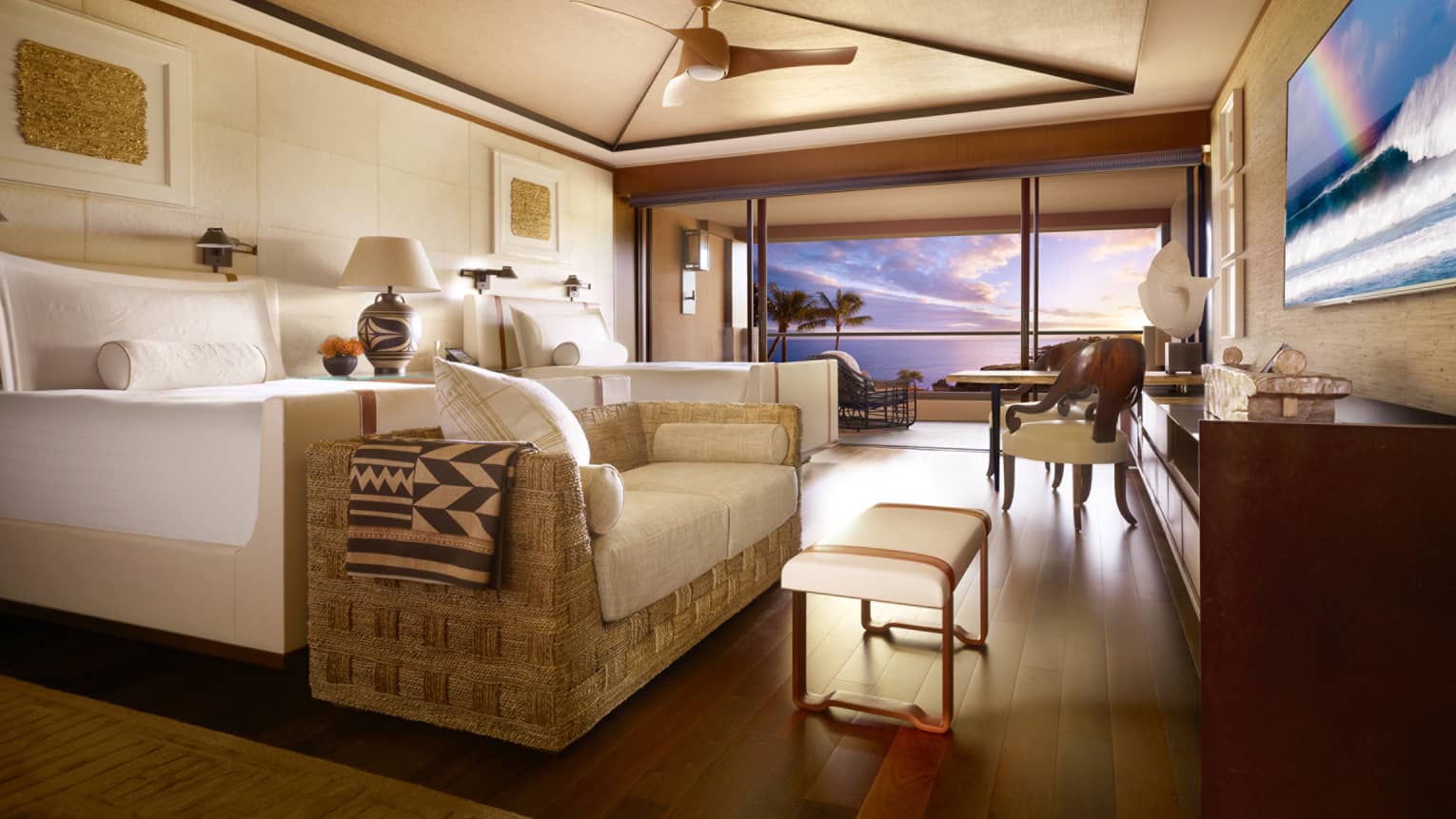 Ocean-View Room bed with loveseat, table at foot by open wall to balcony, sunset