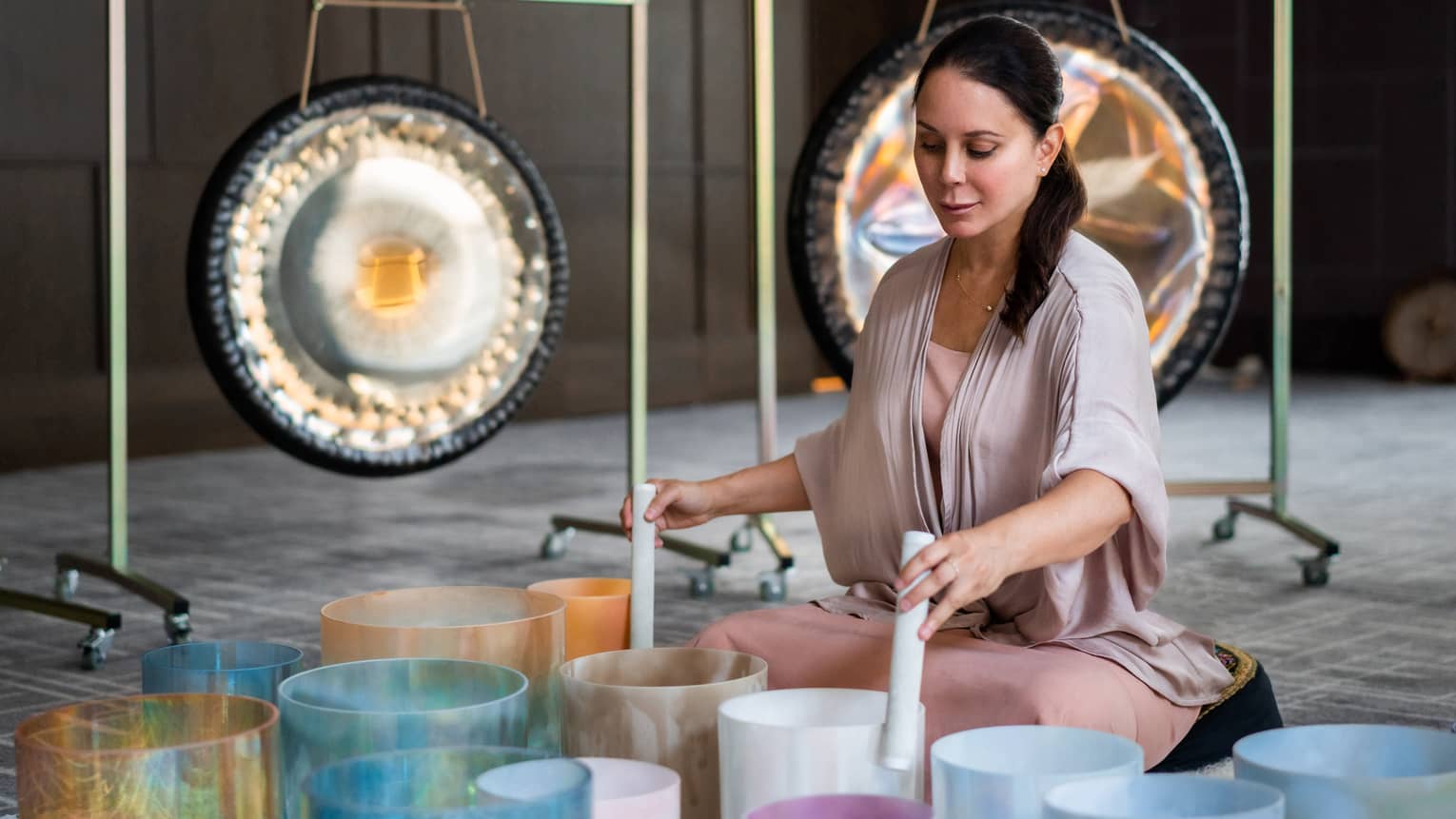 Michelle Pirret playing singing bowls in the foreground with two gongs in the background