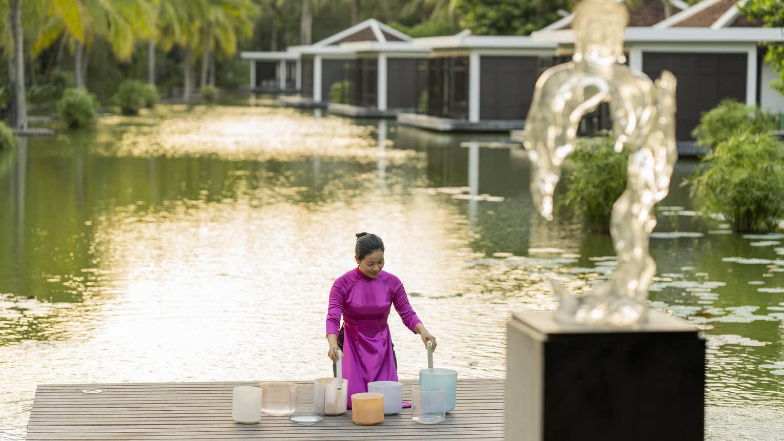 Woman plays crystal singing bowls on the dock of the lake