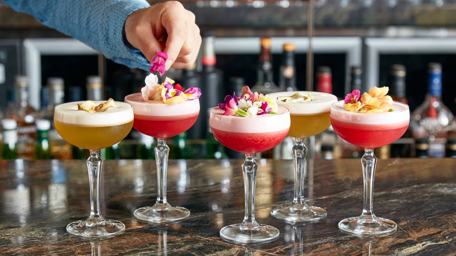 Grain bar mixologist garnishes colourful frozen cocktails with fresh flower petals 