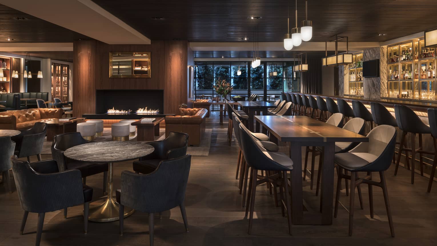 Dark tables and chairs near a large bar with black stools.
