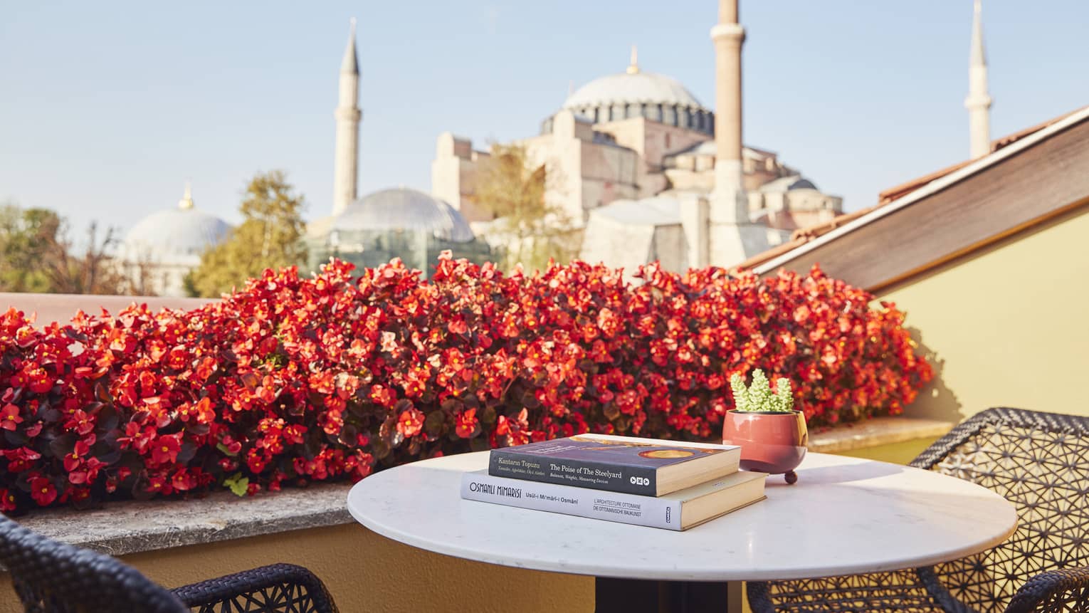 Hotel suite terrace with books on small round table beside red flowers and view of the Blue Mosque