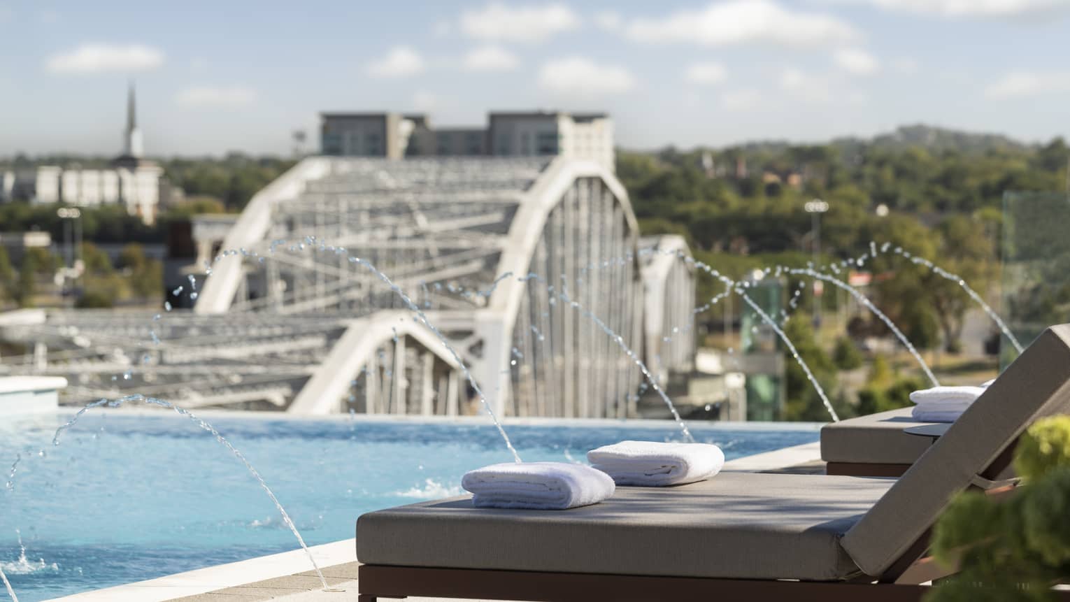 Outdoor pool with water feature, and a city bridge over the river in the background