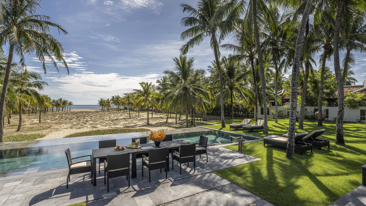 Four Bedroom Pool Villa pool area with dining table, lush green grass, palm trees and blue skies