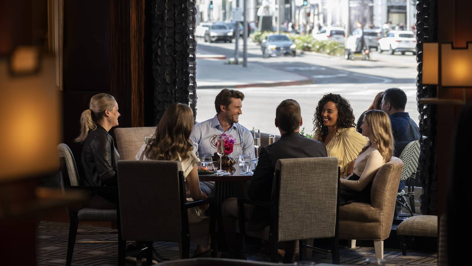 A group of people sitting around a large round table with a view of a road outside.