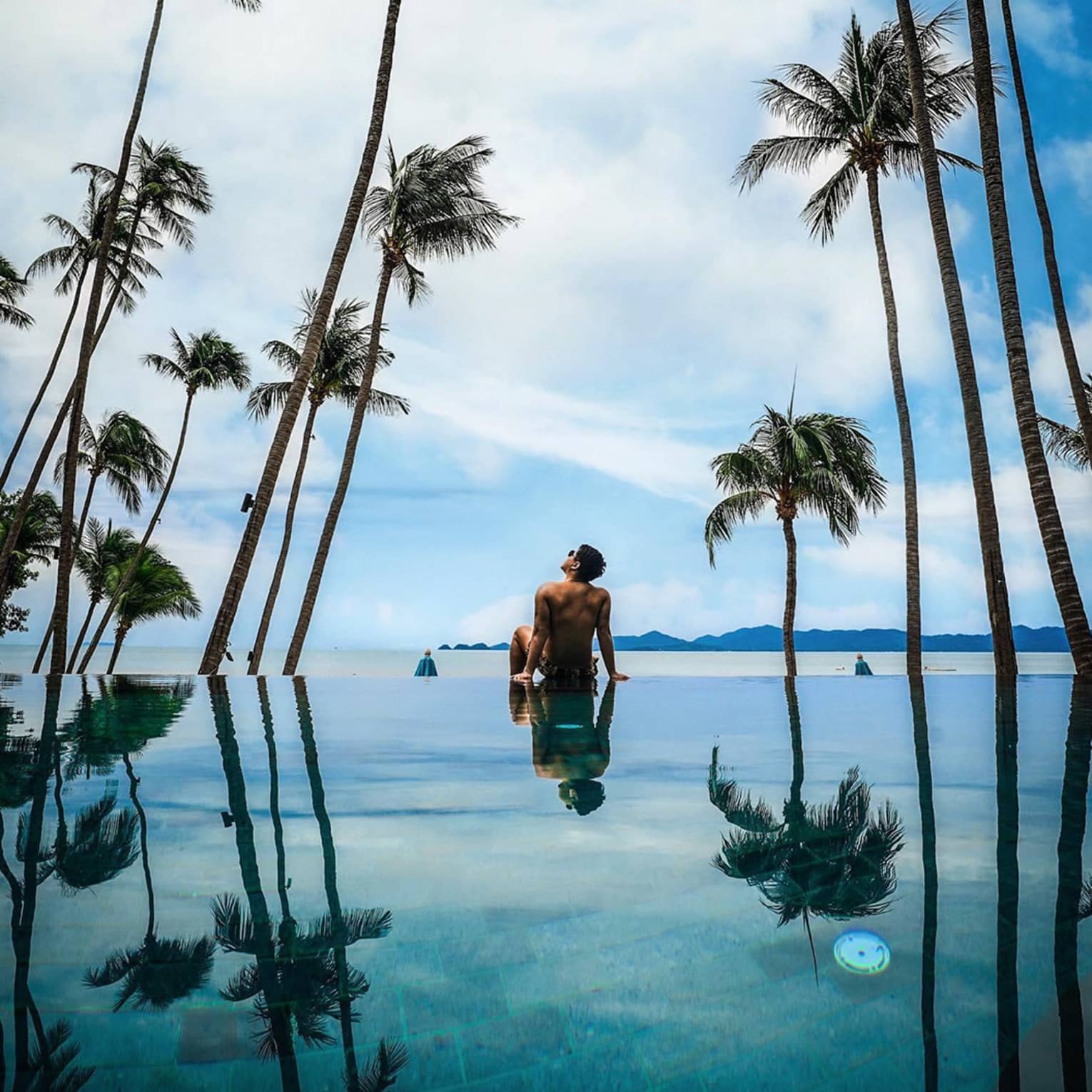 Guest relaxing by the pool surrounded by palm trees