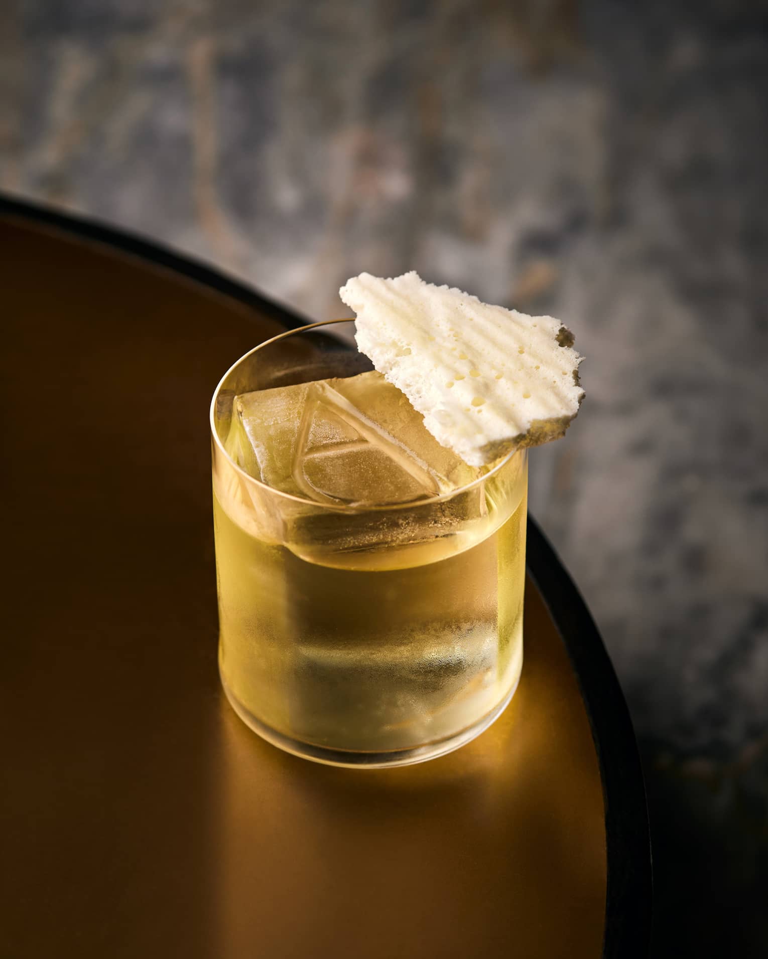 Yellow cocktail in a low glass with a large cube of ice, engraved with the letter A